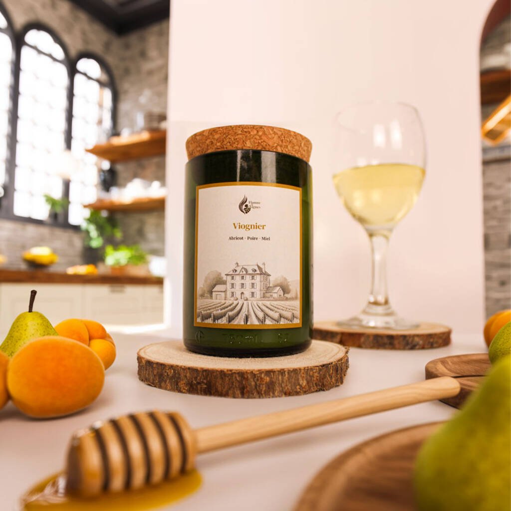 Bougie naturelle Viognier dans une authentique bouteille de vin recyclée verte posée sur un rondin de bois, entourée d'abricots, de poires, d'une cuillère à miel en bois avec du miel coulant et d'un verre de vin blanc.