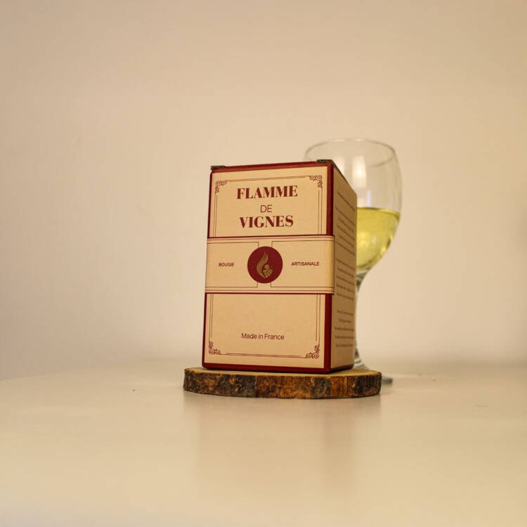 Bougie parfumée artisanale Viognier posée à côté d’une bouteille de vin blanc et de raisins.